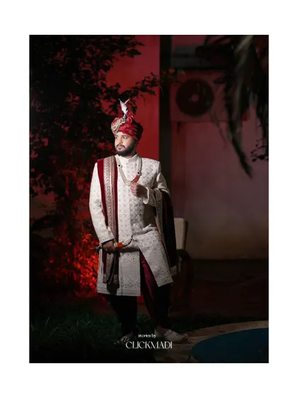 A stylish and dramatic portrait of the groom, his white and red sherwani standing out against the dark background.