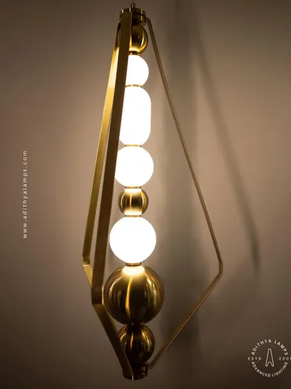 This elegant pendant is framed by a triangular gold structure, enclosing a string of white and gold beads. It's a sophisticated and modern piece that adds a touch of jewelry-like decoration to your space.