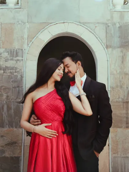 A romantic close-up of the couple. Her makeup is elegant and polished, designed to match the sophisticated look of the one-shoulder red gown.