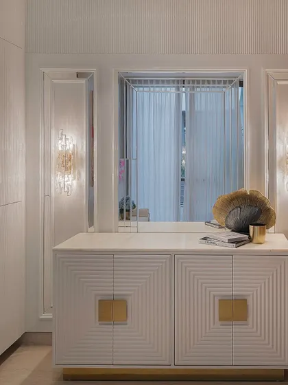 Another angle of the white and gold credenza, showing how it interacts with the wall sconces and mirror behind it. The top provides a perfect surface for displaying curated decor objects.
