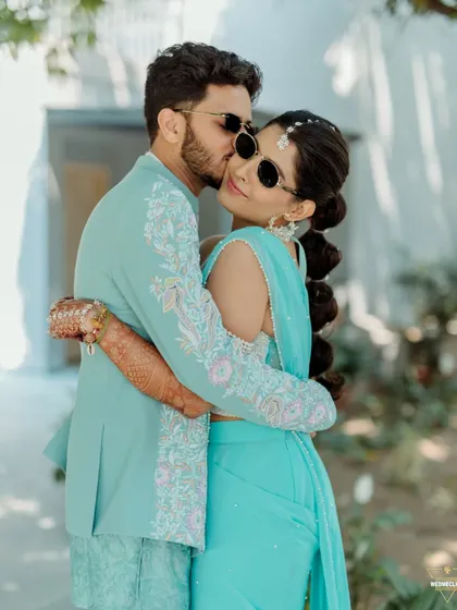 A sweet and stylish kiss on the cheek. The coordinated pastel blue outfits and modern sunglasses give this shot a cool, contemporary feel. It’s a great example of a modern take on a pre-wedding Haldi event shoot.
