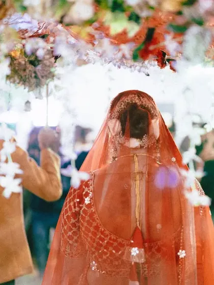 A view of the bride's entry from behind, showing her walking under a beautiful 'phoolon ki chadar'. The soft focus and vibrant colors create a dreamy, artistic photograph of this special procession.