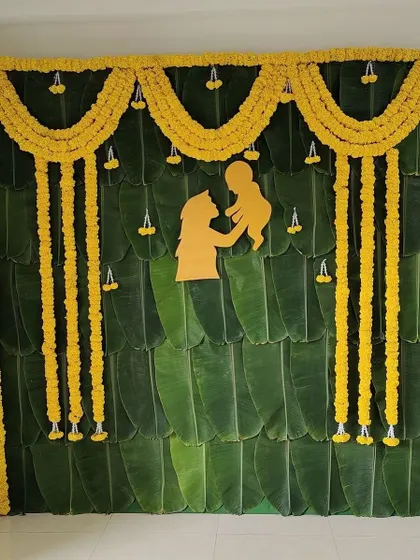 A simple and elegant Seemantham backdrop made entirely of fresh banana leaves. It is adorned with marigold garlands and a central mother and child silhouette, perfect for an intimate home ceremony.