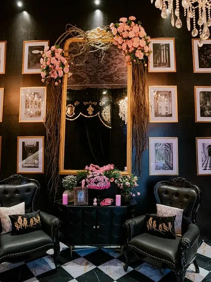 A stylish photo corner with a gallery wall of black-and-white prints. The space is furnished with black leather armchairs and a large, ornate mirror, all set on a classic checkered floor.