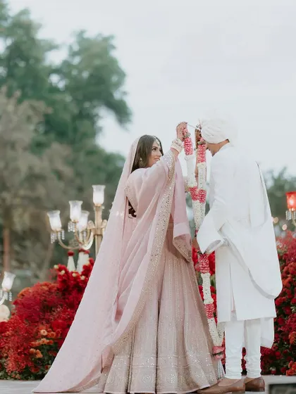 A beautiful moment during the varmala ceremony, with a backdrop of vibrant red flowers and ornate candelabras, showcasing how the decor enhances the key rituals of the wedding.
