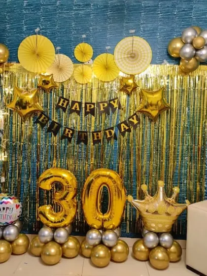 A royal theme for a 30th birthday. This home setup includes a gold shimmer curtain, gold and silver balloons, and a large crown foil balloon.