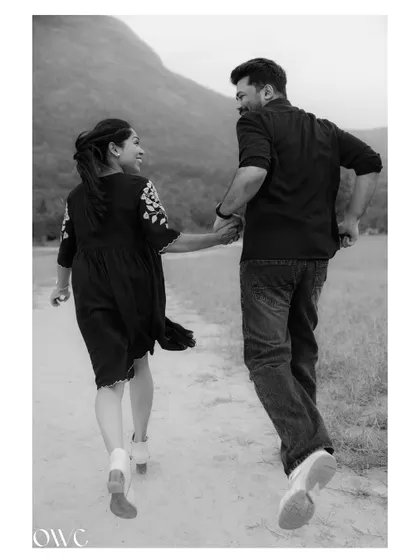 A joyful black and white photo of a couple running along a path, capturing their energy and happiness.