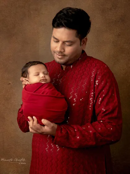 A father dressed in a festive red kurta tenderly holds his sleeping newborn. This photo beautifully captures a moment of quiet connection and cultural pride.