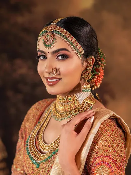A stunning South Indian bridal look featuring a blouse with heavy, multi-colored embroidery. The intricate patterns and rich jewel tones of the threadwork are designed to complement the grand temple jewelry.