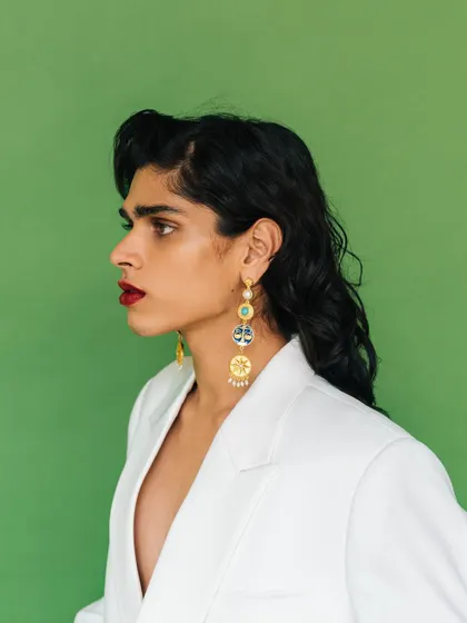 A profile shot for an Amama Jewels campaign. This image highlights the length and detail of the statement earrings against a bold red lip and white blazer.