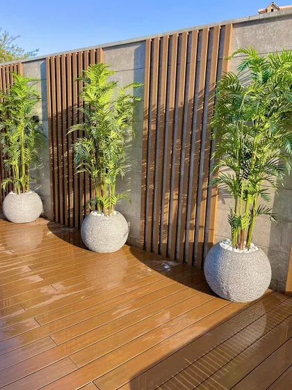A clean and modern patio design with a wooden deck and a feature wall with vertical wood slats. We use large, simple planters with identical plants to create a sense of rhythm and order.