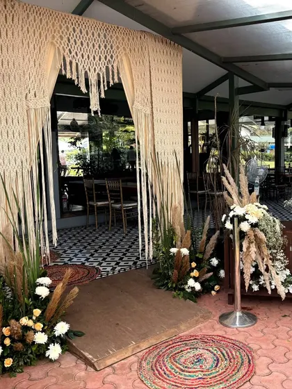 A bohemian-chic Mehendi entrance, featuring a macrame curtain, pampas grass arrangements, and colorful woven rugs for a relaxed and spiritual vibe.