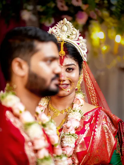 Another angle of the Bengali bride, capturing a candid moment with her groom out of focus in the foreground.