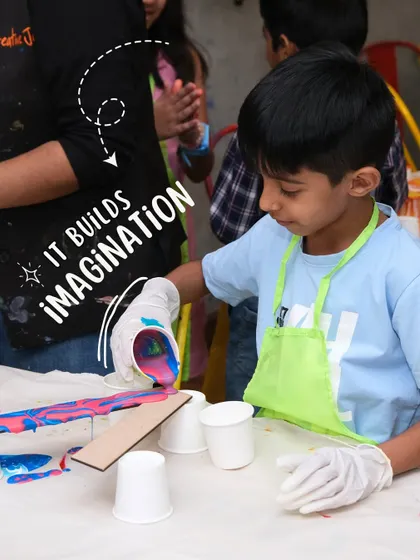 A young boy in an apron is focused on a fluid art project, pouring colorful paint. Art is a wonderful way to build imagination.