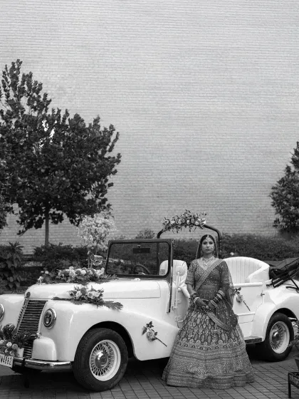 A stunning black and white portrait of the bride standing beside a vintage wedding car. The classic composition and timeless quality make this a truly elegant bridal shot.