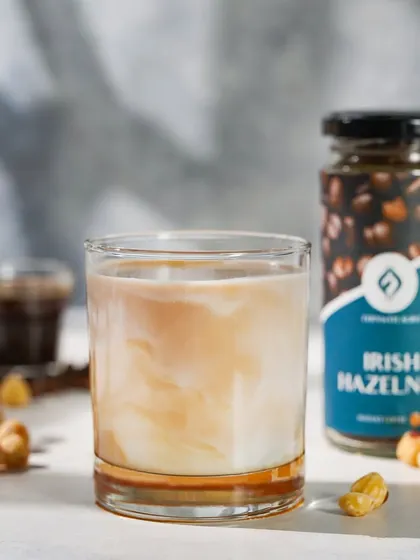 A beautifully layered Irish Hazelnut iced coffee, shot with soft, natural-looking light. The light creates a gentle shadow play that adds depth and a cozy cafe feel to the image.