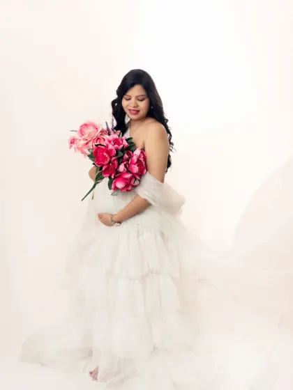 The soft white fabric and a bouquet of bright pink flowers create a lovely, fresh look for this maternity portrait.
