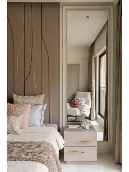 This shot highlights the details of the bedroom, including the full-length mirror that reflects the seating area and adds depth to the room. The bedside table with its clean lines and gold hardware is both stylish and functional.