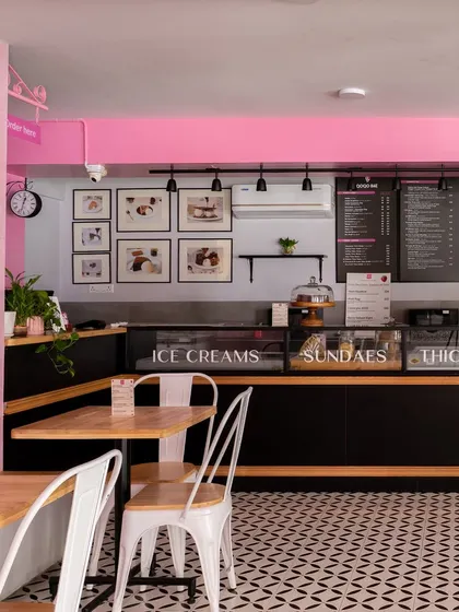 The service counter and menu display at Qoqobae. The design integrates functionality with the overall aesthetic, using clean black counters to ground the space and framed art to add a personal, curated touch.