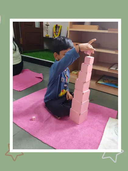 The pink tower stands tall, built with care and precision by Ishan. This is a proud moment, showcasing his concentration and control of movement.