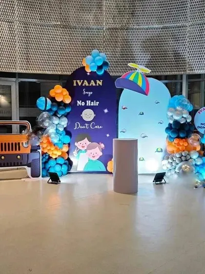 A unique and funny "No Hair Don't Care" Mundan or first birthday party theme. This setup includes custom arched backdrops with cartoon graphics, a jeep cutout, and balloon arrangements.