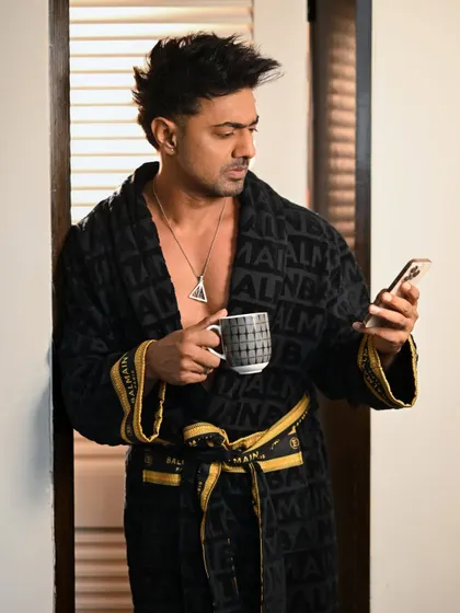 A candid moment with Dev in a bathrobe, checking his phone. This behind-the-scenes style shot feels personal and offers a glimpse into a more relaxed, off-camera persona.