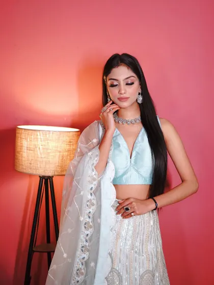 A close-up of the white and blue lehenga, showing the delicate embroidery and the simple, elegant jewelry it pairs with.