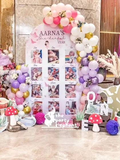 A wonderful milestone board celebrating Aarṇa's first year, integrated into the butterfly fairyland theme with surrounding props and balloons.