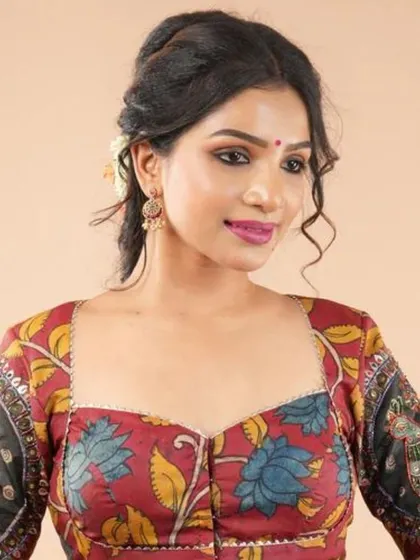 This blouse showcases a beautiful floral Kalamkari print on a maroon base with a sweetheart neckline. The sleeves feature a contrasting black panel with traditional motifs.