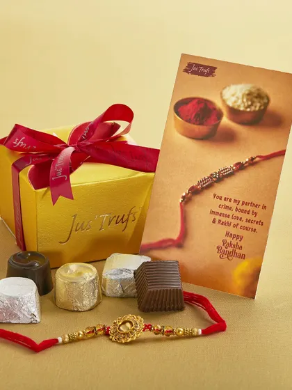 Our small gold gift box is tied with a red ribbon, with wrapped chocolates, a Rakhi and a card beside it.