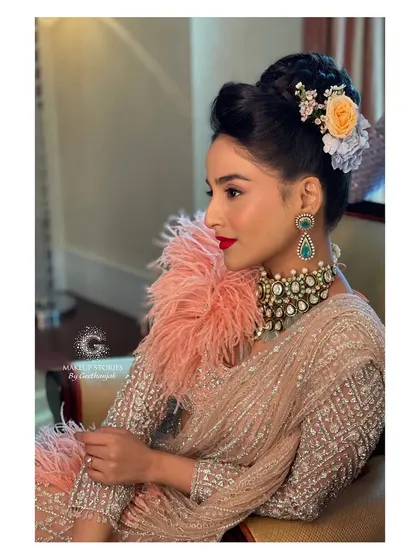 A side profile of Krishna's cocktail look, showing the elegant updo adorned with flowers. The makeup is flawless, with a focus on radiant skin and a striking lip color.