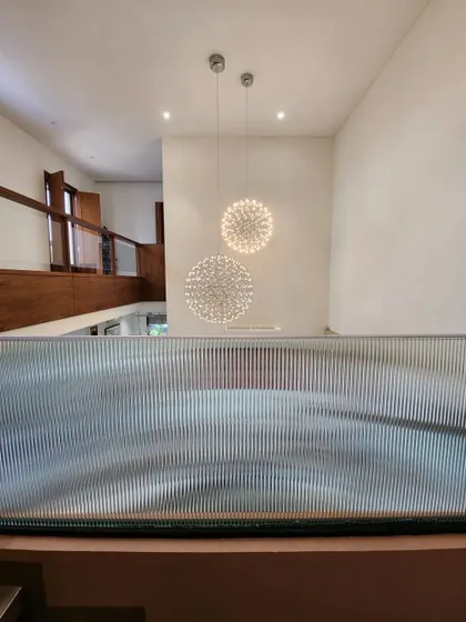 Looking down from the upper level, this view captures the sculptural quality of the fluted glass railing and the cascading effect of the spherical chandeliers. This detail shows how we play with texture and light to connect different floors.