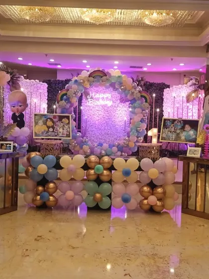 A wide view of a lavish birthday party stage. The setup includes a central circular balloon wreath, two shimmer walls, and multiple character cutouts like Boss Baby and Frozen's Elsa.