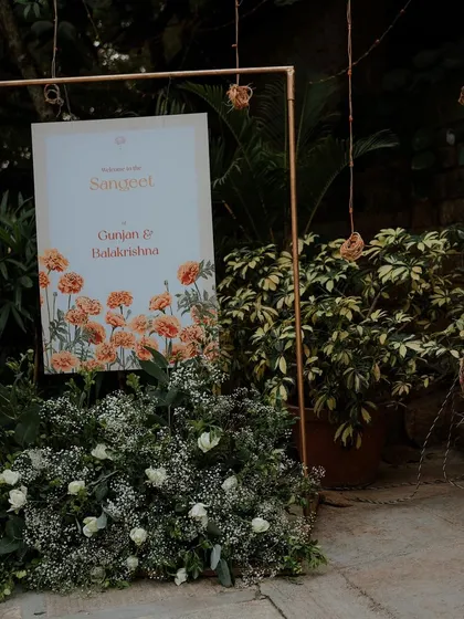 A welcome sign for the Sangeet, framed in copper and adorned with baby's breath and white roses.