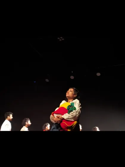 A performer holds a collection of colorful clothes, a poignant symbol in our dance theatre production 'Sea's Fire'.