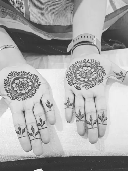 This black and white photo highlights the clean lines of a simple mandala design. Paired with leafy motifs on the fingers, it's a beautiful and understated choice.