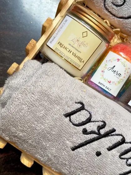 A close-up of a wedding hamper showing the personalized towel, a French vanilla aromatherapy candle, and my special rainbow bath salts. It's a perfect blend for a soothing spa experience at home.