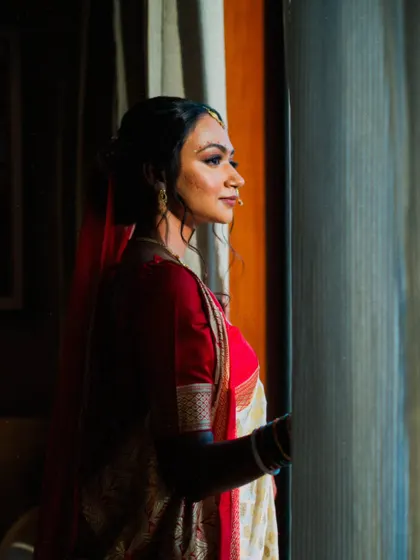 A beautifully composed portrait of a bride in a traditional saree, looking out the window with a thoughtful expression.