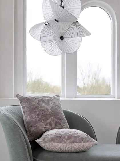 A close-up of the Serpentine Light, showing its delicate, fan-like paper structure against a window, emphasizing its translucency and lightness.
