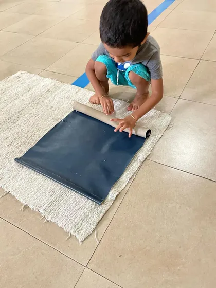 At the end of a work period, a child carefully rolls up his work mat. This simple action reinforces the full cycle of an activity: preparation, work, and cleanup.