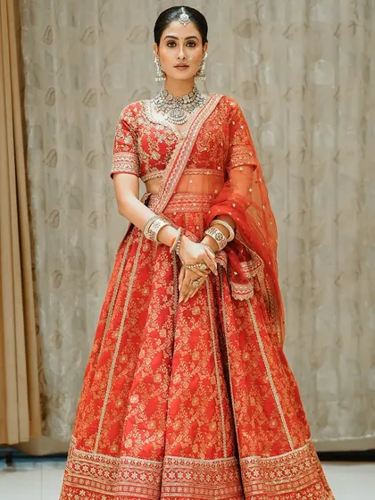A full-length shot of a stunning red bridal lehenga. The makeup is bold and regal, with diamond jewelry adding a touch of modern glamour to the traditional outfit.