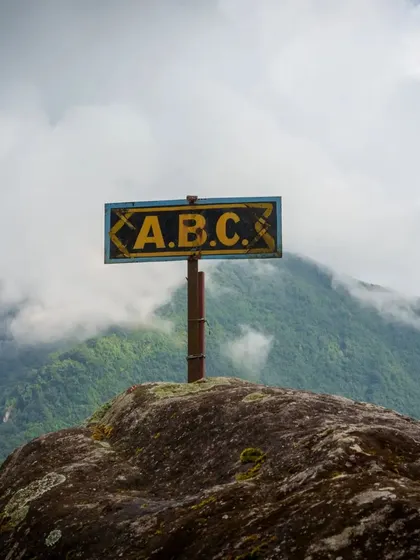 The iconic A.B.C. sign marks a key point on the trail, with the misty green mountains of the Annapurna Sanctuary rising in the background.
