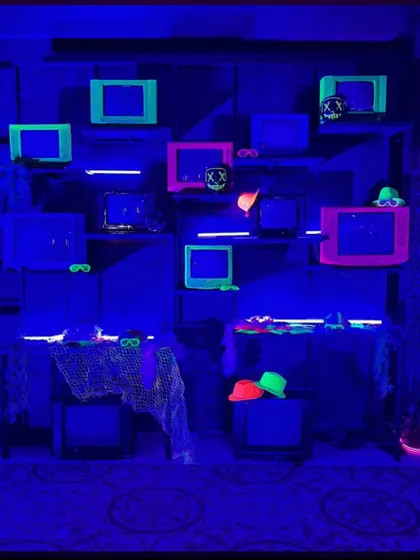 A retro-themed photo booth we designed for a neon party. We built a wall of vintage television sets, accenting them with neon-outlined frames and props like glowing masks and hats for guests to use.