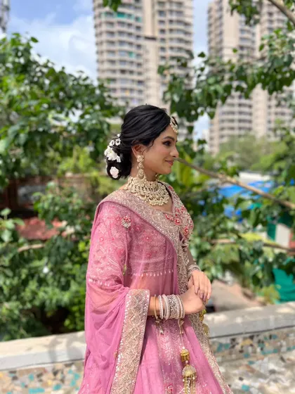 This bride's sangeet makeup was designed for a daytime celebration. The subtle elegance of the look enhances her features without being overpowering, perfectly matching her pink lehenga and the outdoor setting.