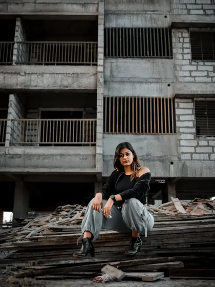 A commanding pose with the model seated, looking directly at the camera, exuding confidence in the middle of the industrial setting.