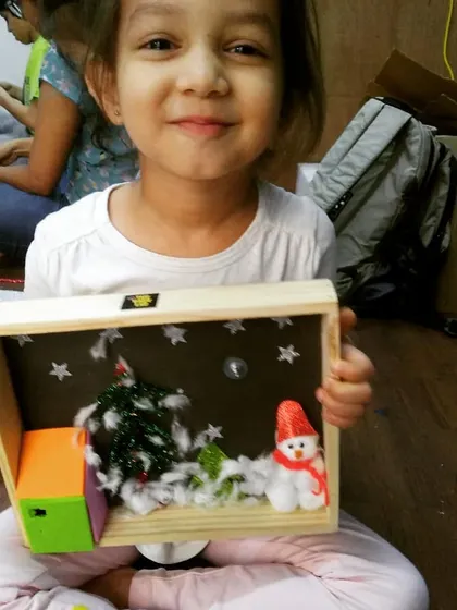 A proud student shows off her Christmas-themed diorama, complete with a snowman and a light-up element. It's a perfect example of a fun, seasonal STEAM project.