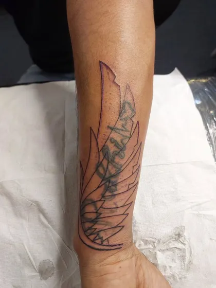 Before: The outline of a new wing design is stenciled over an old script tattoo on the forearm.