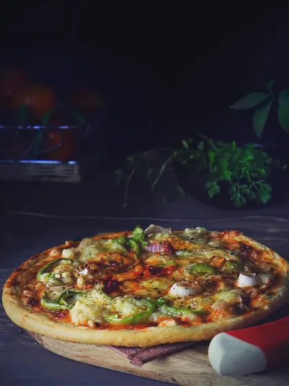 A full, home-baked pizza sits on a wooden board in a dark, rustic setting. The moody lighting makes the melted cheese and fresh toppings look extra comforting and delicious.