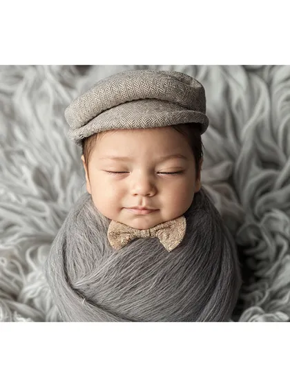 A dapper little gentleman, this newborn is dressed in a flat cap and bow tie for a classic, timeless portrait.