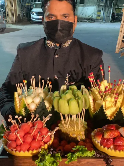 A server presenting an elaborate platter of intricately carved fresh fruit. We turn simple fruit into a visual spectacle with melon balls, pineapple skewers, and sculpted watermelon bowls.